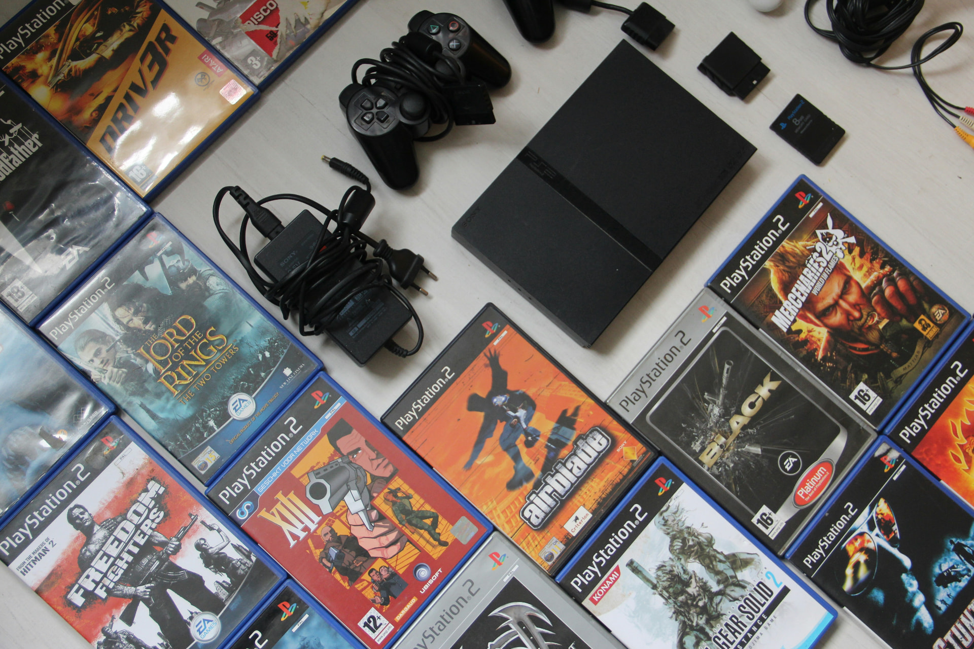 PlayStation 2 console, controllers and dozens of boxed PS2 games laid out on a table